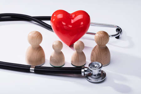 Close-up Of Wooden Pawns, Red Heart Shape And Stethoscope On White Background