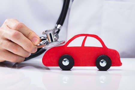 Close-up Of A Doctor's Hand Examining Red Car With Stethoscopeの写真素材