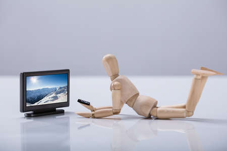 Side View Of A Wooden Lying On Floor Dummy Watching Television Over White Backgroundの写真素材
