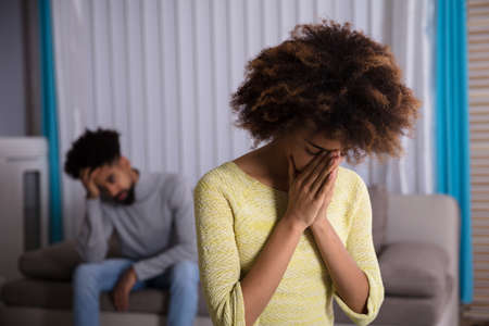 Close-up Of An Unhappy Young Woman In Front Of Man Sitting On Sofaの写真素材