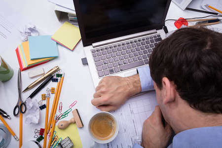 Close-up Of Exhausted Businessman Leaning His Head On Laptop Over The Messy Desk At Workplaceの写真素材