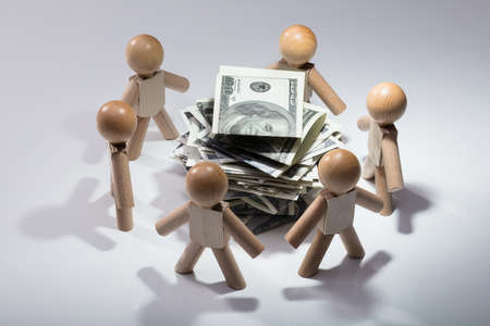 Stacked Banknotes Surrounded By Wooden Human Figures On White Backgroundの写真素材