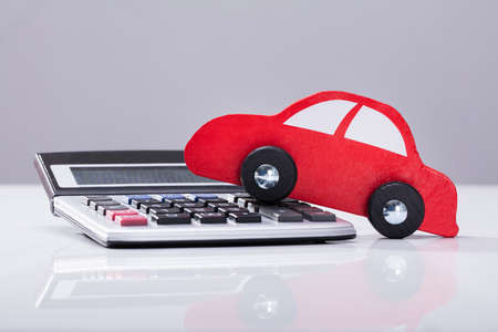 Close-up Of Red Car And Calculator Against Grey Backgroundの写真素材