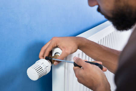 Close-up Of A Young Male Plumber Installing Radiator With Screwdriverの写真素材