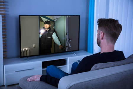 Young Man Sitting On Sofa Watching Suspense Movie On Televisionの写真素材