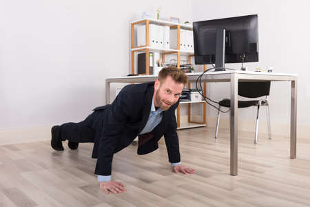 Young Businessman Doing Pushups On Hardwood Floorの写真素材