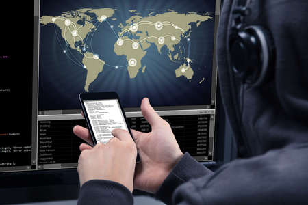 Hacker Using Mobile Phone For Stealing Data From Computer Screen Showing World Mapの写真素材