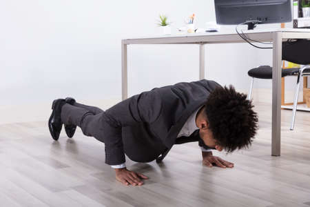 Young Businessman Doing Push Up On Floor At Workplaceの写真素材