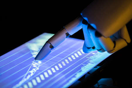 Close-up Of A Robot's Hand Using Digital Tablet With Financial Graphs On Screenの写真素材