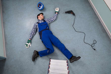 Elevated View Of Unconscious Handyman Lying On Floor With Helmet And Drill