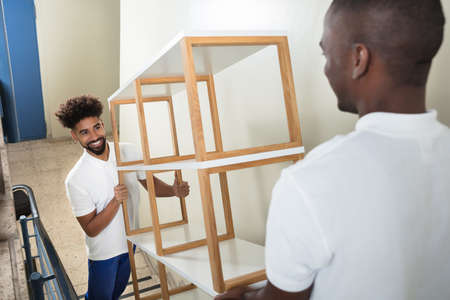 Two Male Movers Carrying The Empty White Shelf On The Staircase At Homeの写真素材