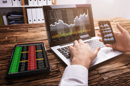Close-up Of A Stock Market Broker Working With Graphs On Laptop At Workplace