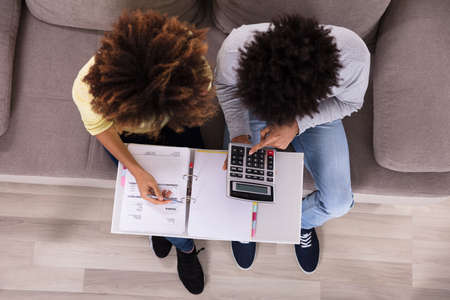 High Angle View Of Young Couple Sitting On Sofa Analyzing Billの写真素材