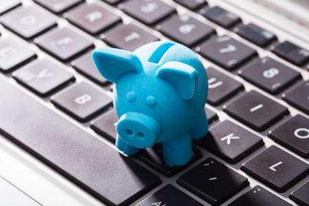 Close-up Of Small Blue Piggybank On Laptop Keypadの写真素材