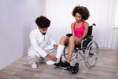 Male Physiotherapist Examining Leg Of Female Patient Sitting On Wheelchairの写真素材