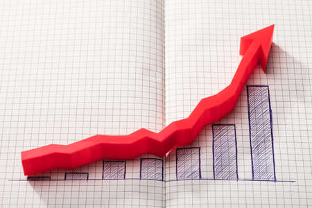 Elevated View Of Red Arrow Over Increasing Graph On Chequered Notebook