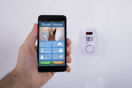 Human Hand Using Mobile Phone In Front Of Security System Mounted On Wallの写真素材