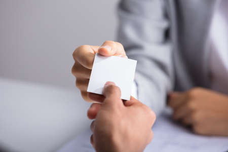 Close-up Of Businessperson's Hand Giving Blank White Card To Partnerの写真素材