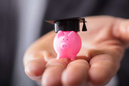 Close-up Of A Businessperson's Hand Holding Piggybank With Graduation Capの写真素材