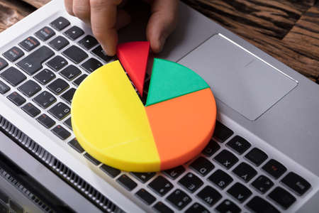 Close-up Of A Human Hand Placing Last Piece Into Pie Chart Over Laptop Keypadの写真素材