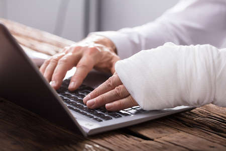 Close-up Of A Businessperson's Hand With Hand Injury Using Laptop