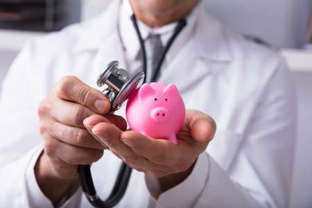 Close-up Of A Doctor's Hand Checking Pink Piggybank With Stethoscopeの写真素材