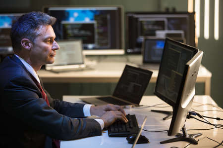 Side View Of A Mature Businessman Working On Multiple Computers In Office