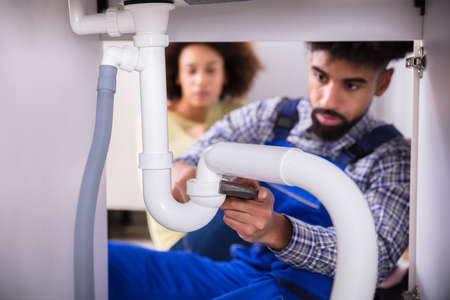 Close-up Of A Male Plumber Fixing Sink Pipe In Kitchen