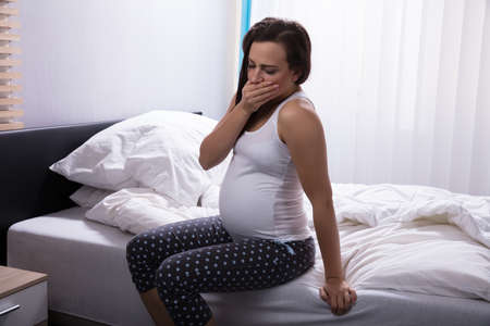 Side View Of A Young Woman Sitting On Bed In Bedroomの写真素材