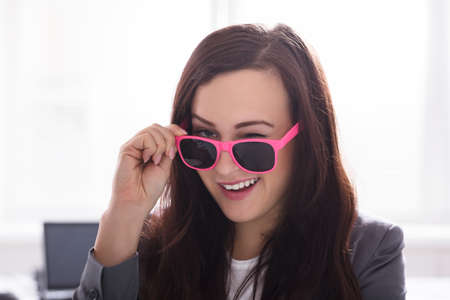 Portrait Of A Young Businesswoman Wearing Pink Sunglasses In Officeの写真素材