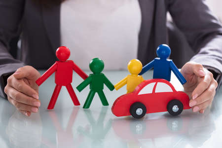 Close-up Of A Businessperson's Hand Protecting Multi Colored Human Figures And Red Carの写真素材