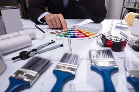 Architect's Hand Choosing Color From Swatch With Paint Brushes On Blueprint