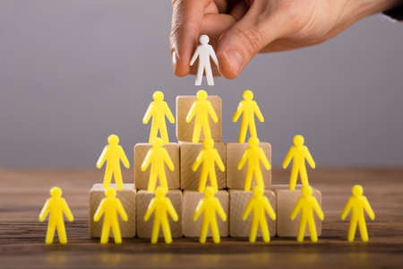 Close-up Of A Person Placing White Human Figure Standing On Top Of Yellow Human Figuresの写真素材