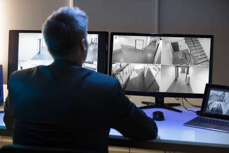 Side View Of A Mature Businessman Looking At CCTV Camera Footage On Multiple Computer Screen