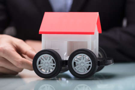 Close-up Of A Person's Hand Holding House Model On Cart Over The Deskの写真素材