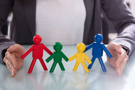 Close-up Of A Businesswoman's Hand Protecting Multi Colored Human Figures At Workplace