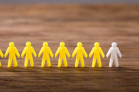 White Figure Standing Among Yellow Human Figures In A Row On Wooden Backgroundの写真素材