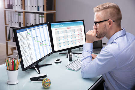 Side View Of A Young Businessman Looking At Gantt Chart On Computer In Office