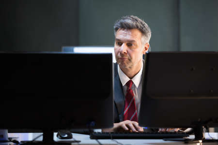 Mature Businessman Multiple Computers At Office Deskの写真素材