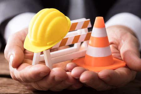 Close-up Of Human Hand Holding Barricade With Traffic Cone And Hard Hatの写真素材