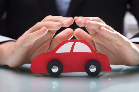 Close-up Of A Businessperson's Hand Protecting Red Car On Desk At Office