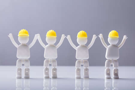 Close-up Of Human Figures With Yellow Hard Hat Standing Against Grey Background