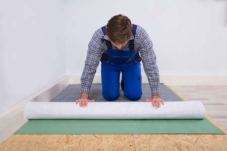 Side View Of A Young Male Worker In Overalls Installing Carpetの写真素材