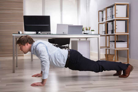 Side View Of A Young Businessman Doing Push Up In Officeの写真素材