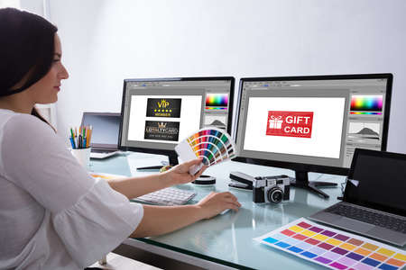 Female Designer Holding Color Swatch Working With Gift Card On Computer Screenの写真素材
