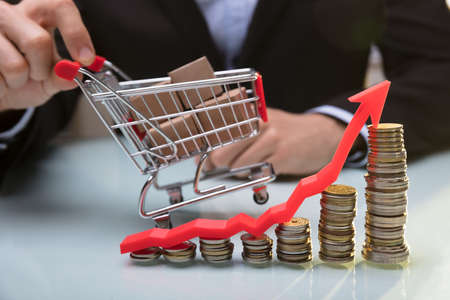 Stacked Coins And Arrow Showing Upward Direction In Front Of Businessperson Holding Shopping Cartの写真素材