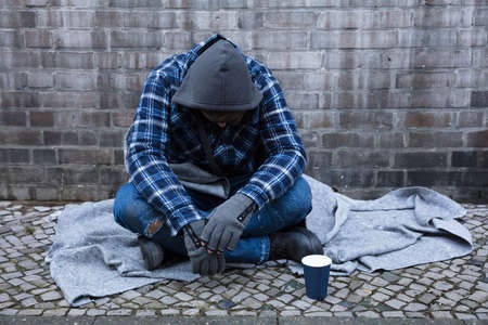 Side View Of A Male Beggar Sitting On Street Near Disposable Cupの写真素材