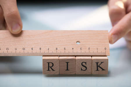 Close-up Of A Businessperson's Hand Measuring Risk Blocks With Wooden Rulerの写真素材