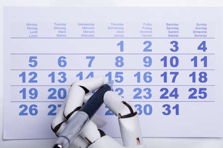 Close-up Of A Robotic Hand Marking Date On Calendar With Penの写真素材