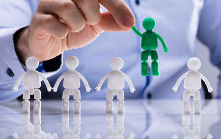 Close-up Of A Person's Hand Selecting Green Figure Amongst White Human Figures In A Rowの写真素材